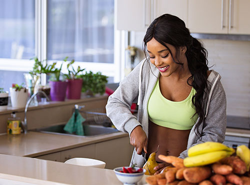 A woman cutting fruit in the kitchen with other vegetables.