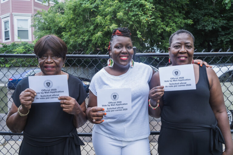 Three women holding up papers in front of a fence.