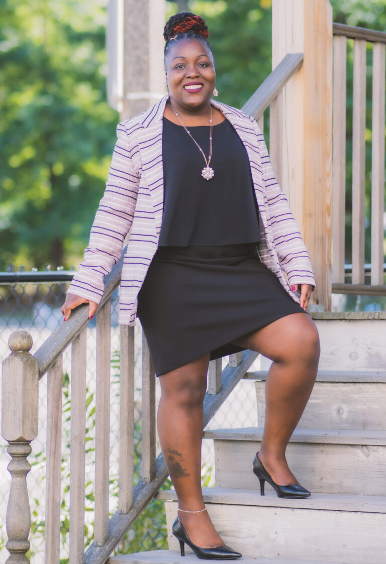 A woman in black dress and striped jacket on steps.