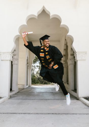 A man in graduation attire jumping into the air.